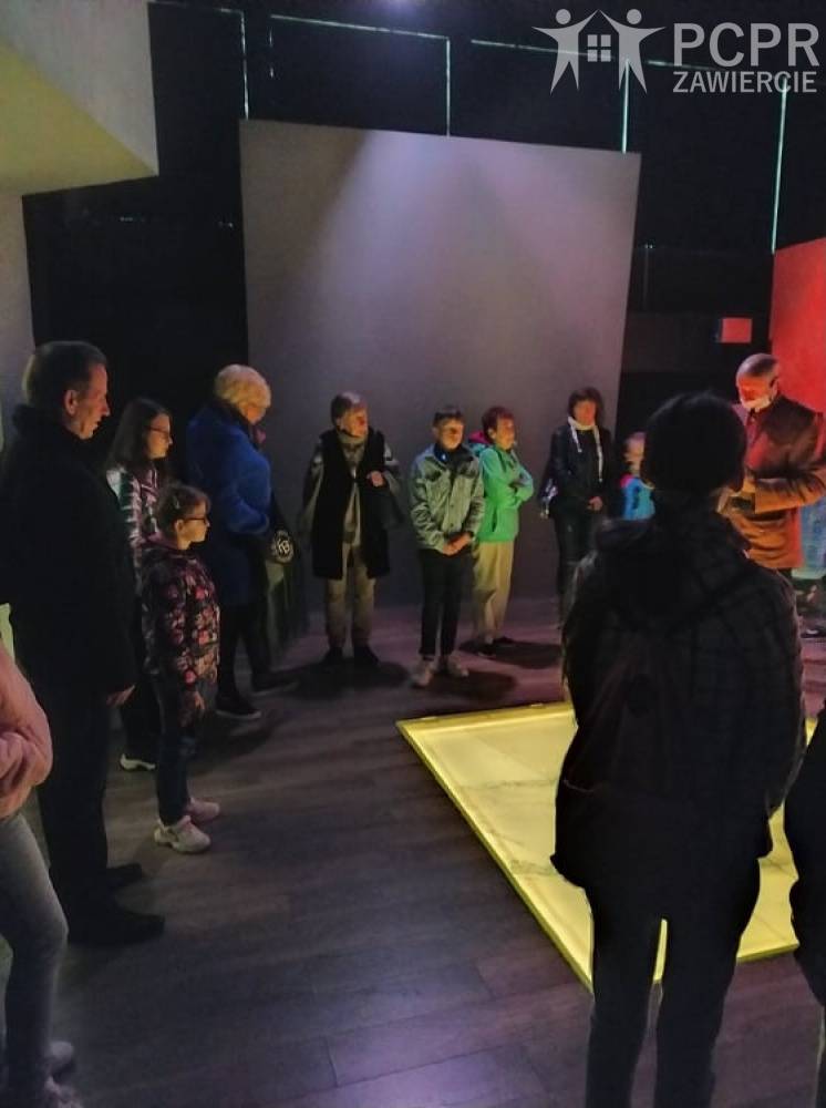 Zdjęcie: Grupa osób stoi w pomieszczeniu muzealniczym wokół podświetlonego w podłodze obiektu